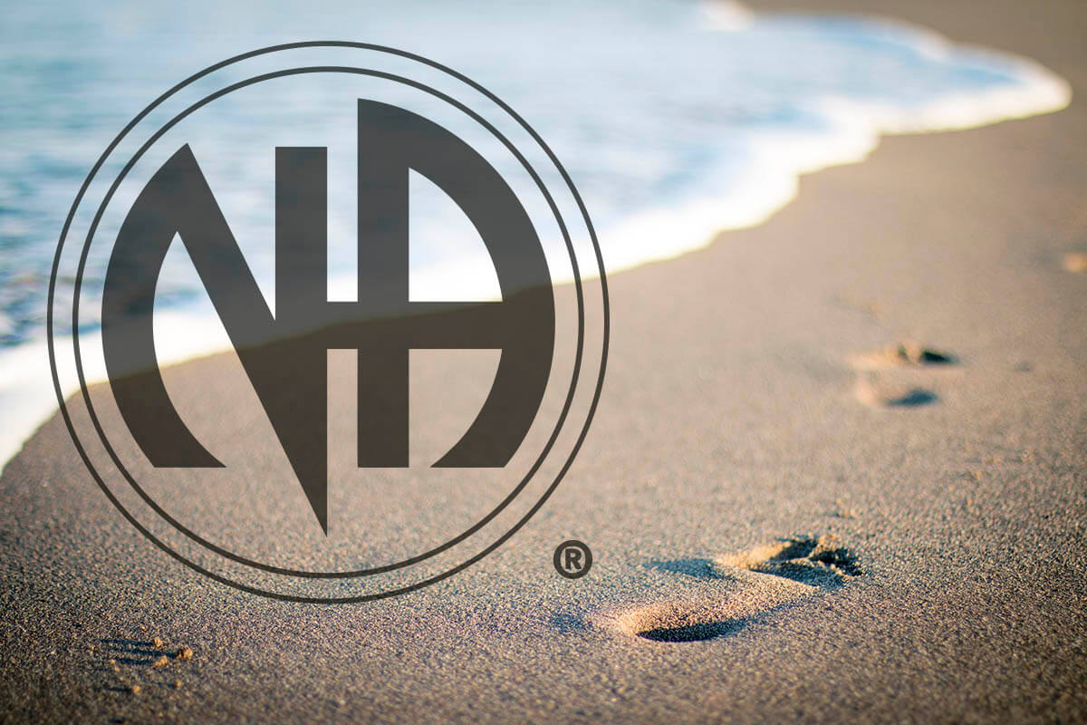 Imagem de pegadas na praia com o logotipo de Narcóticos Anônimos em destaque, simbolizando os doze passos.